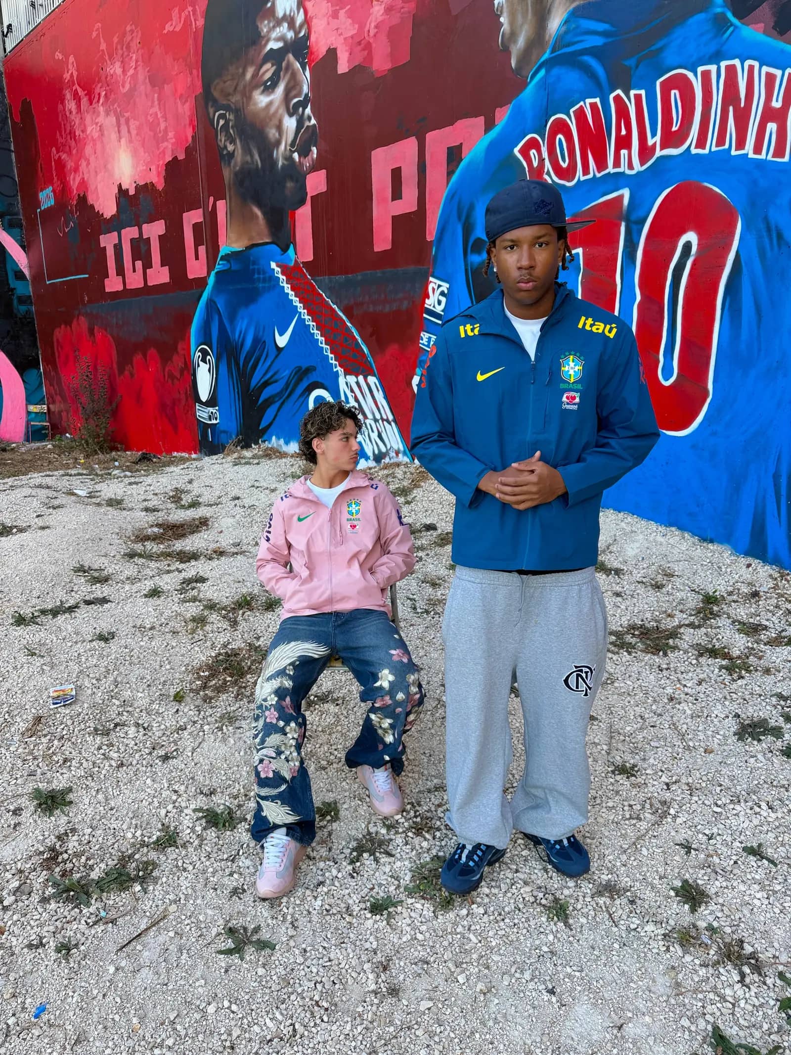 Deux clients Drip Seleção en veste Brasil rose et veste Brasil bleue devant une fresque street art