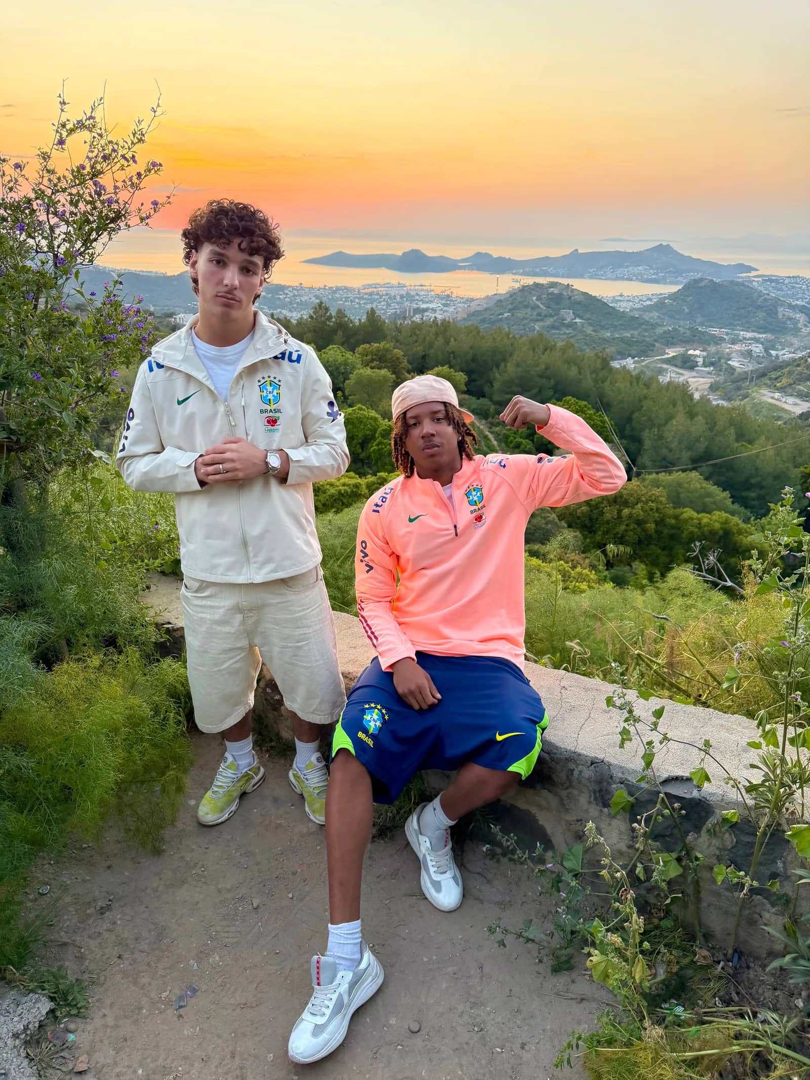 Deux clients Drip Seleção en veste imperméable blanche et pull zippé rose saumon, baie de Rio au coucher du soleil