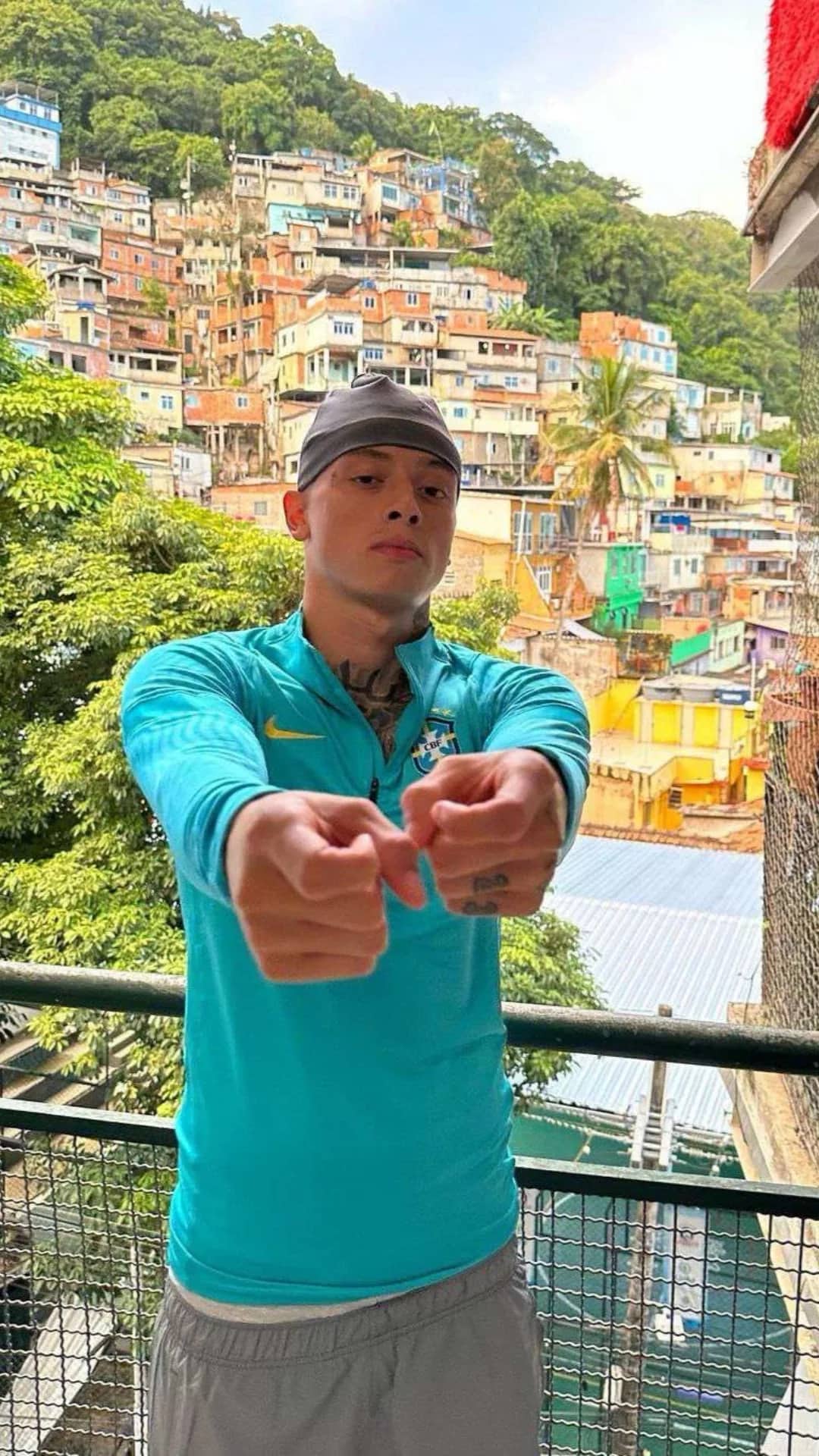Homme portant le pull zippé bleu turquoise Brésil, favela de Rio en arrière-plan