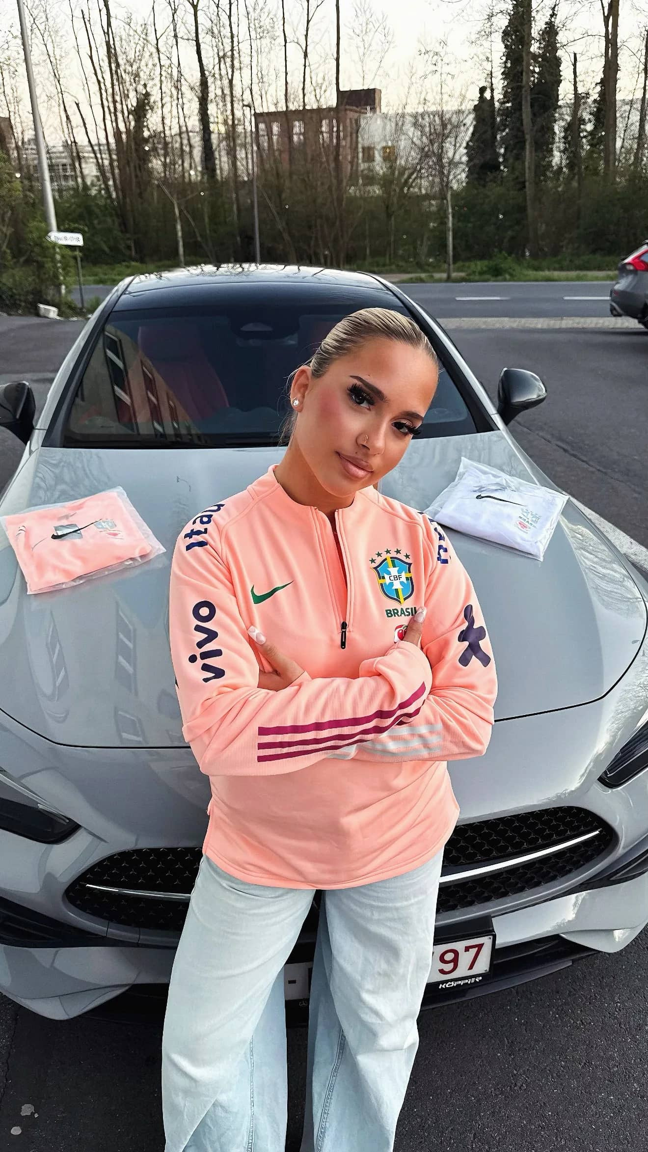 Femme portant le pull zippé rose saumon Brésil, appuyée contre une voiture blanche