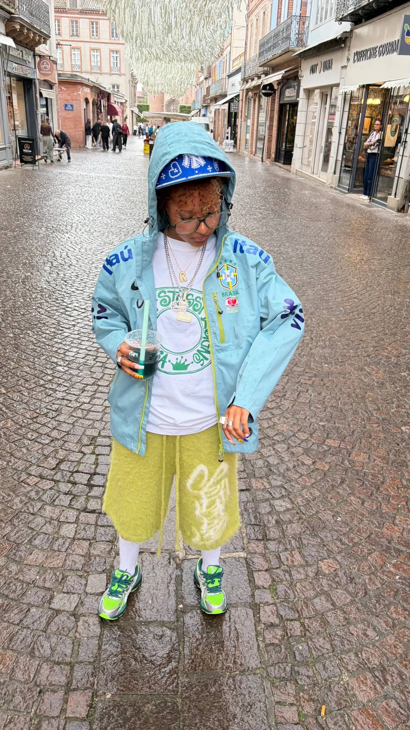 Veste du Brésil bleu ciel portée capuche relevée dans une rue pavée
