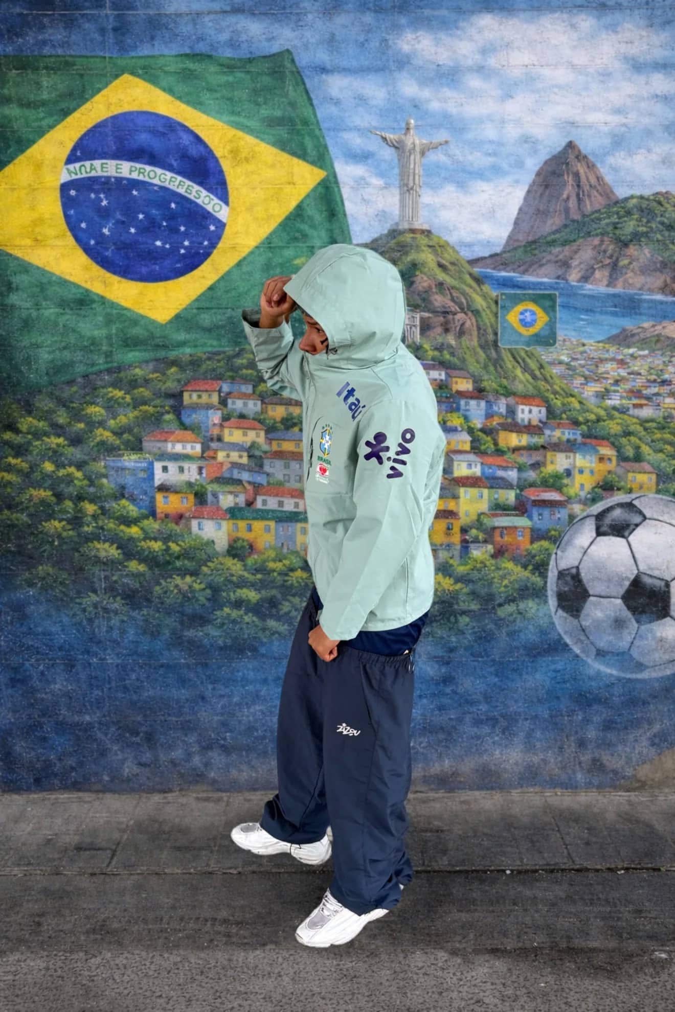 Veste imperméable du Brésil verte portée devant une fresque du drapeau brésilien et du Corcovado